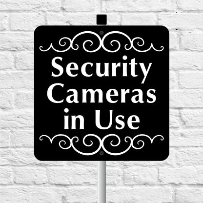 Black and white 'Security Cameras in Use' sign on a white brick wall background