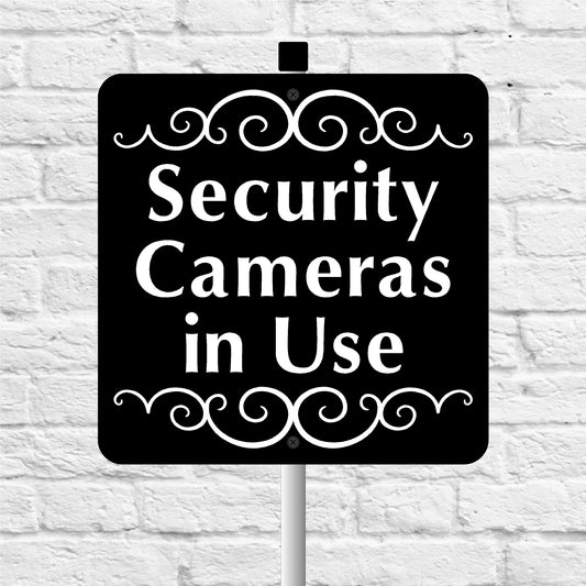 Black and white 'Security Cameras in Use' sign on a white brick wall background