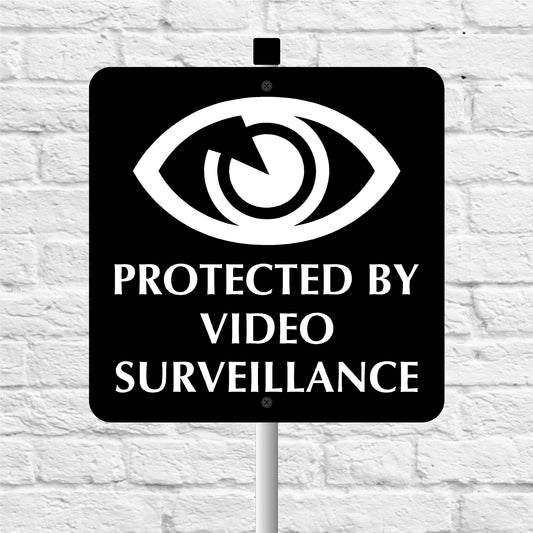 Sign with eye symbol and 'Protected by Video Surveillance' text on a white brick wall background
