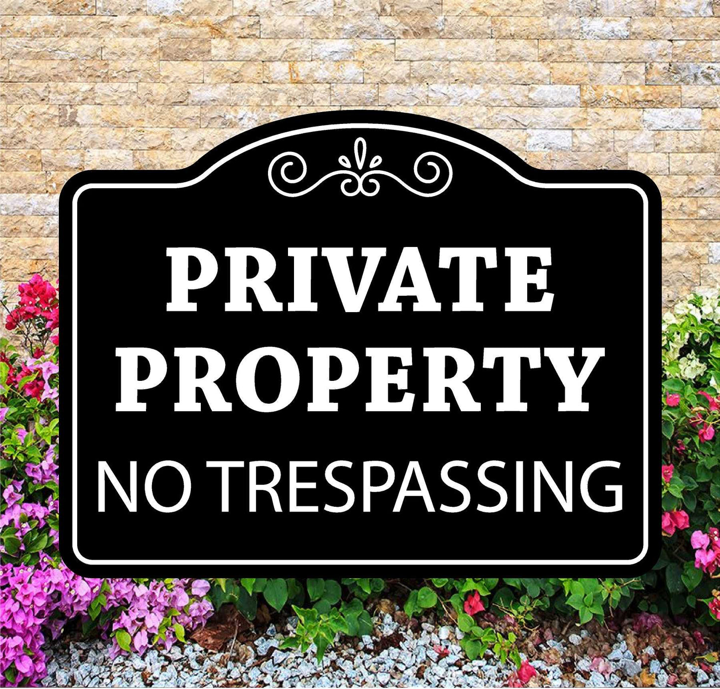 Black and white 'Private Property No Trespassing' sign in front of a stone wall and flowers.