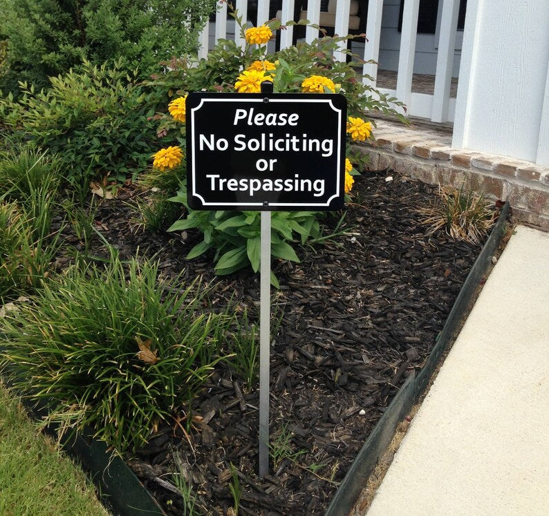 No Soliciting or Trespassing sign in a garden setting with yellow flowers and greenery.